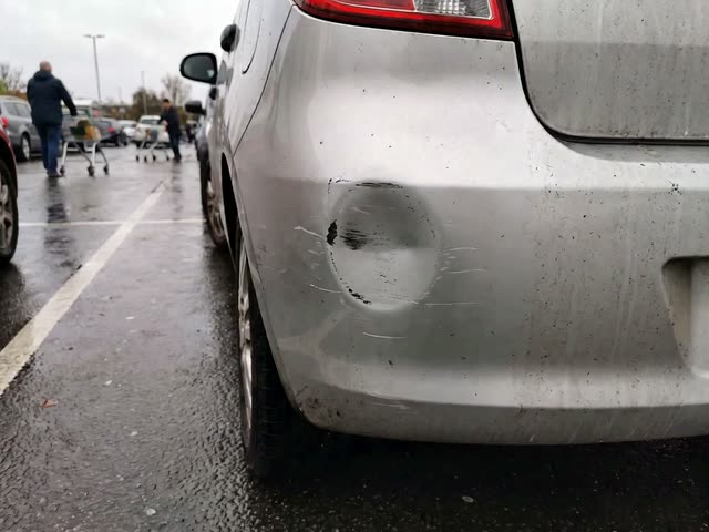 A dent with scraped paint on a car's rear bumper